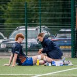 A sports therapist tends to an injured athlete on an outdoor football field.