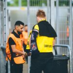 Security personnel and a fan at a football stadium checkpoint in Dortmund, Germany.