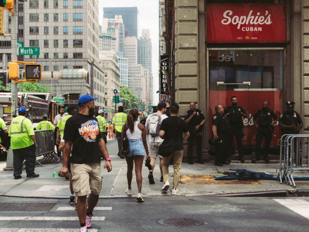 A vibrant street corner in New York City with pedestrians and police officers in the summer.