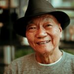 Warm portrait of a smiling elderly man wearing a hat, indoors with soft lighting.
