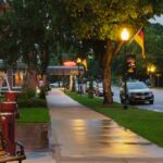 A serene evening street scene in Wabasha, MN, showcasing lit lamps and a wet pathway.