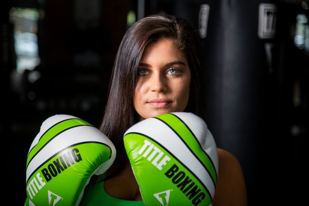 Portrait of a determined female boxer with green gloves indoors, ready for training.