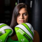 Portrait of a determined female boxer with green gloves indoors, ready for training.