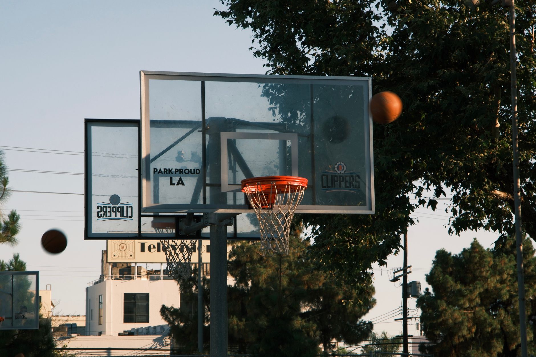 A basketball hoop on an outdoor court in Los Angeles, with trees and buildings in the background.
