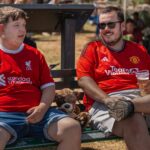 Two football fans wearing rival jerseys discussing at a public outdoor event.