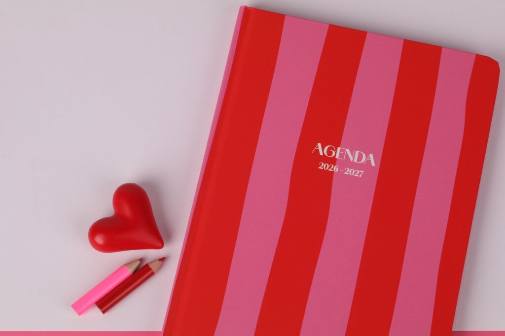 Colorful agenda with red and pink stripes, heart, and pencils on a flat lay.