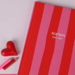 Colorful agenda with red and pink stripes, heart, and pencils on a flat lay.