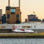 View of airplanes parked at London City Airport with industrial buildings in the background at sunset.