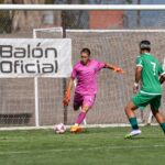 Goalkeeper in pink uniform and player in green during intense soccer match outdoors.