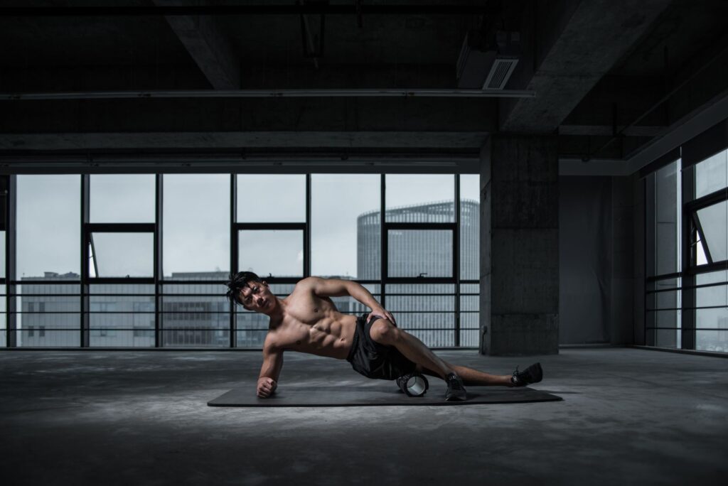Muscular man performing yoga stretch indoors on a mat with urban window view in the background.