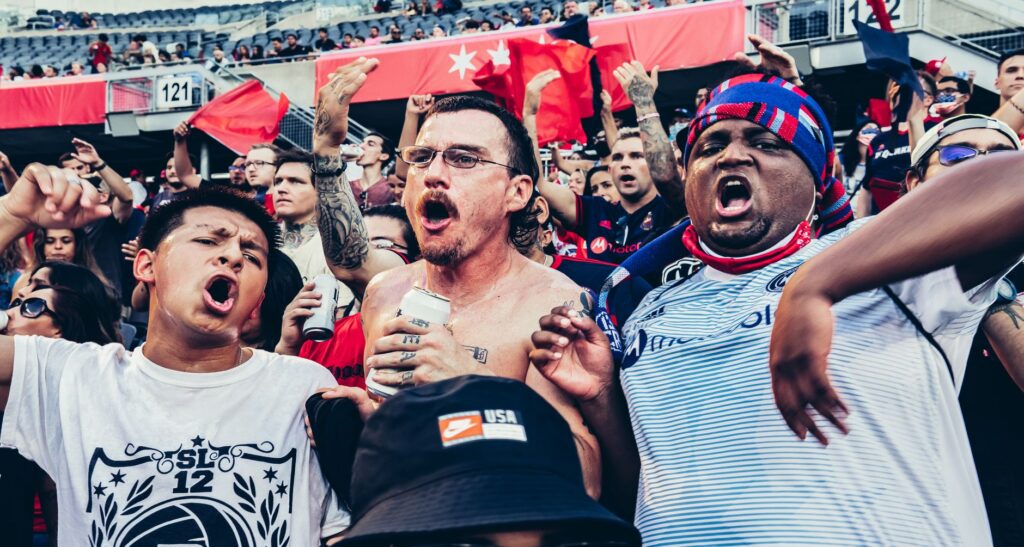 A rowdy group of football fans cheers in a crowded stadium, showcasing excitement and spirited celebration.