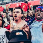 A rowdy group of football fans cheers in a crowded stadium, showcasing excitement and spirited celebration.