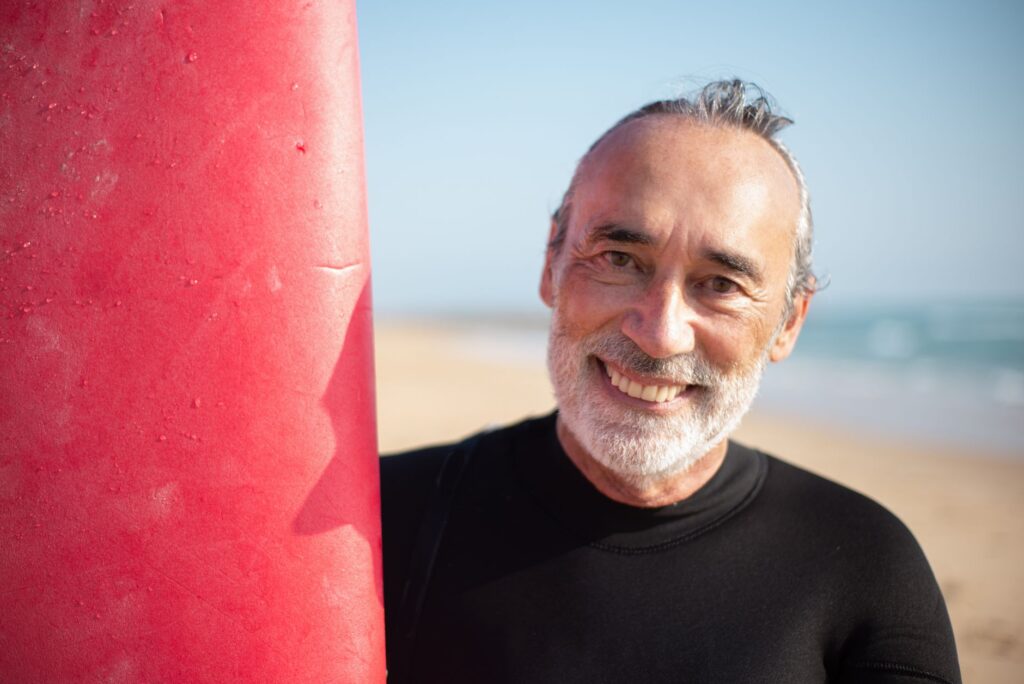 Elderly man with a surfboard enjoying a sunny day at a Portuguese beach.