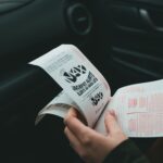 Close-up of hands holding Lotto Max papers inside a car, symbolizing luck and chance.