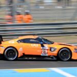 A bright orange Aston Martin on the Le Mans circuit, captured during a motorsport endurance race.