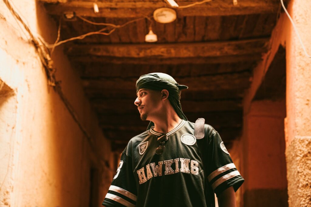 A young man wearing a bandana explores a rustic, dimly lit alleyway.