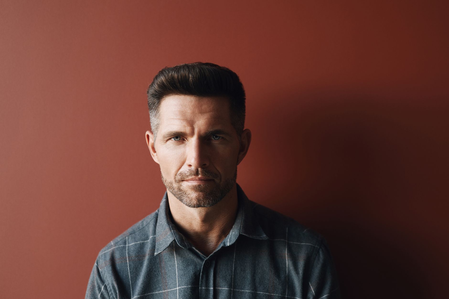 Studio portrait of an adult man with facial hair against a dark background.