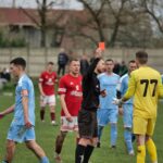 A heated moment as a referee shows a red card to a goalkeeper during a competitive soccer match.