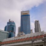 View of Singapore's skyline, featuring skyscrapers and the historic Fullerton Hotel under a cloudy sky.