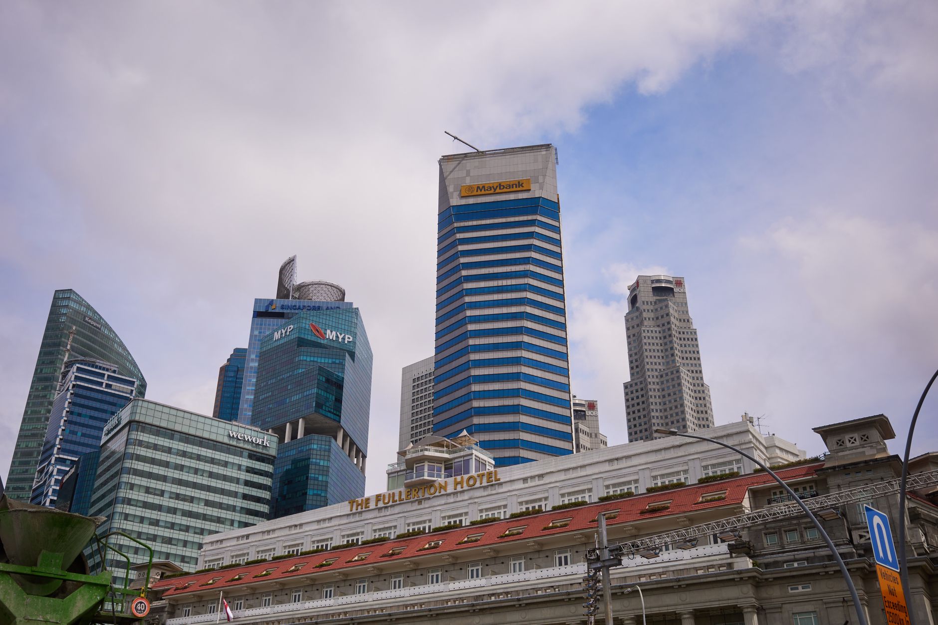 View of Singapore's skyline, featuring skyscrapers and the historic Fullerton Hotel under a cloudy sky.