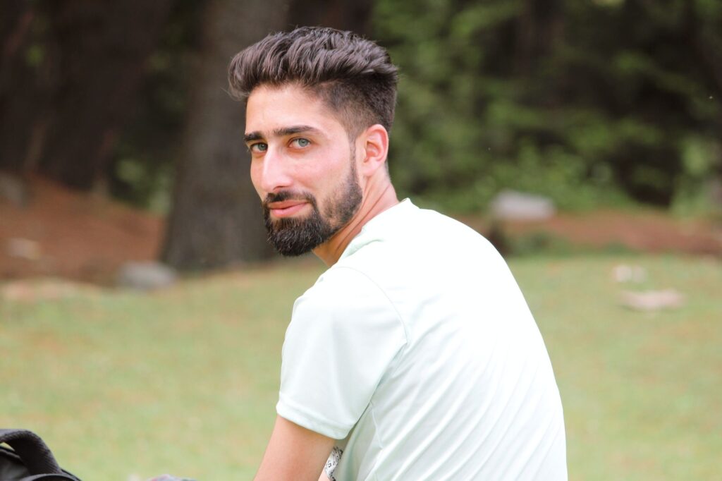 Portrait of a bearded man in white shirt looking over shoulder outdoors in Srinagar.