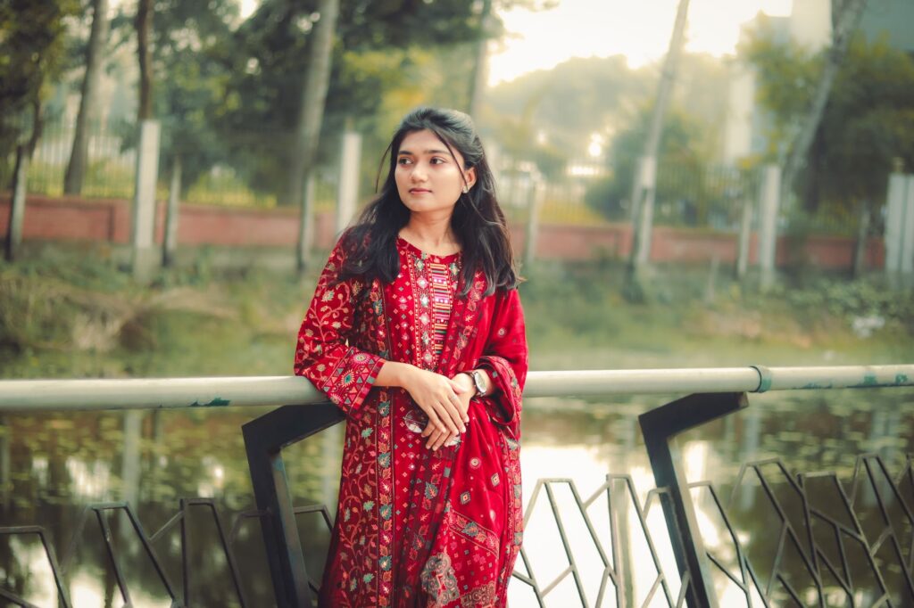 A young woman in vibrant traditional attire stands by a serene lake in Khulna, Bangladesh.