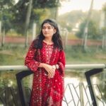 A young woman in vibrant traditional attire stands by a serene lake in Khulna, Bangladesh.
