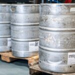 Image of metal beer kegs on wooden pallets in an indoor brewery setting, ideal for industrial storage themes.