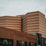 A perspective view of modern brick buildings with horizontal patterns under a cloudy sky.
