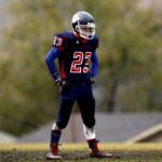 Athlete in full gear standing on football field, helmet and uniform visible.