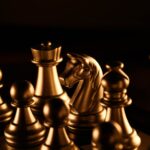 Dramatic close-up of golden chess pieces on a chessboard under warm lighting.