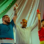 A referee declares the winner of an indoor boxing match, raising their arm in victory.