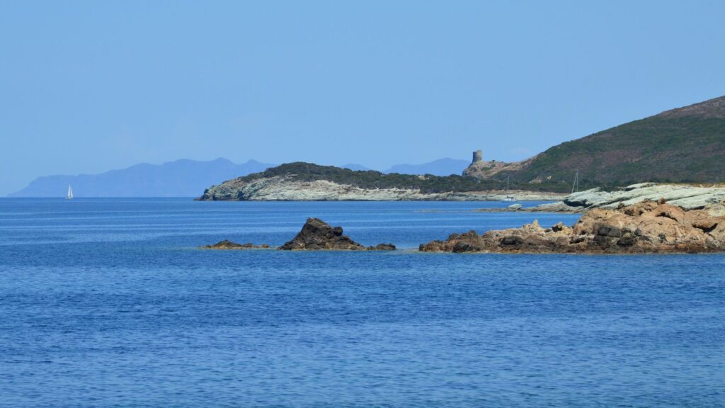 Beautiful seascape of Ersa, Corsica with rocky coast and sailboat under clear summer skies.