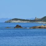 Beautiful seascape of Ersa, Corsica with rocky coast and sailboat under clear summer skies.