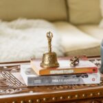 Close-up of a decorative bell and books on a carved wooden table in a cozy setting.