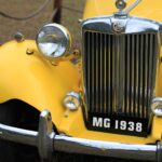 Close-up photograph of a vintage yellow MG 1938 car showcasing its front grill and headlights.