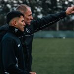 A soccer coach discusses strategy with a young player during outdoor training.