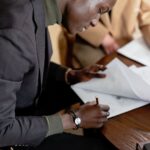 African American man focused on signing important business documents at a desk.