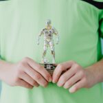 A person holding a silver soccer trophy against a blue background.