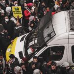 A crowd of protesters surrounding a police van holding signs during a demonstration against Israeli occupation.