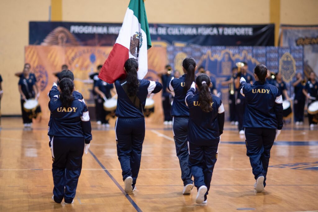 Indoor school sports event featuring students carrying the Mexican flag with pride.