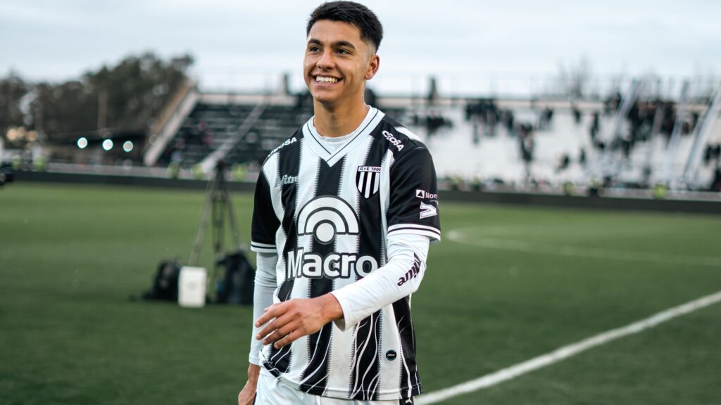 Young soccer player in team uniform smiling during a match on a field.