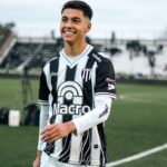 Young soccer player in team uniform smiling during a match on a field.