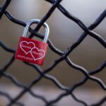 A red love padlock with names on a chain link fence, symbolizing eternal love.
