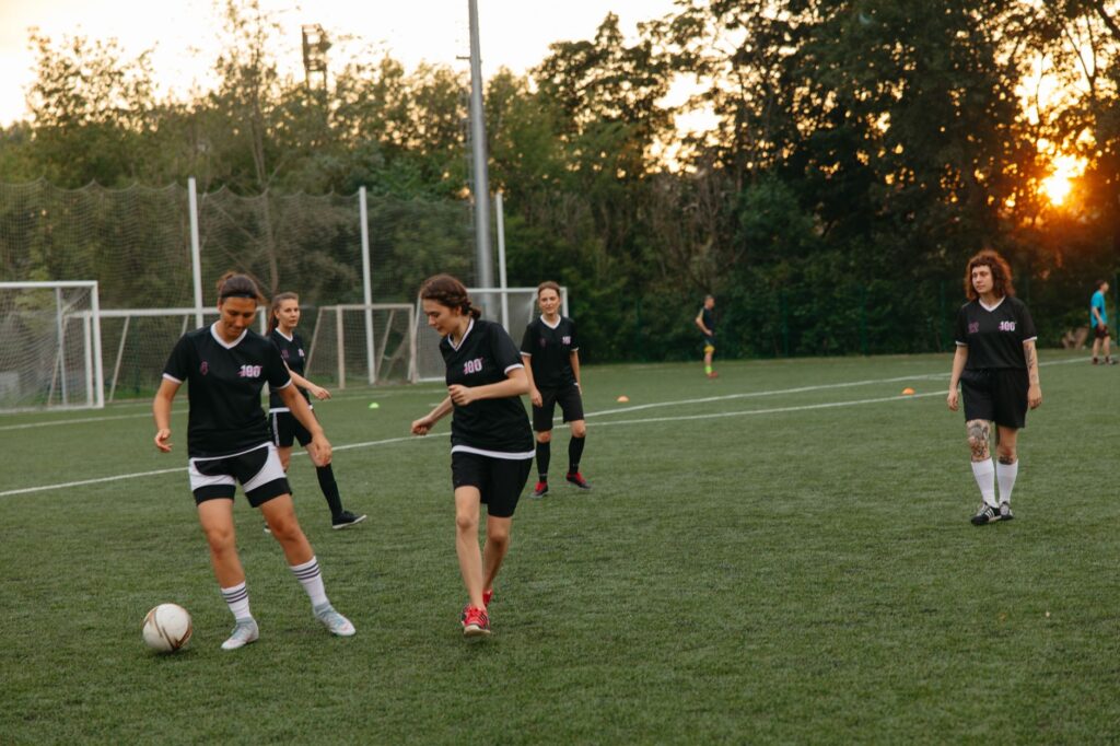 Women soccer players practice on a field at sunset, showcasing teamwork and athleticism.