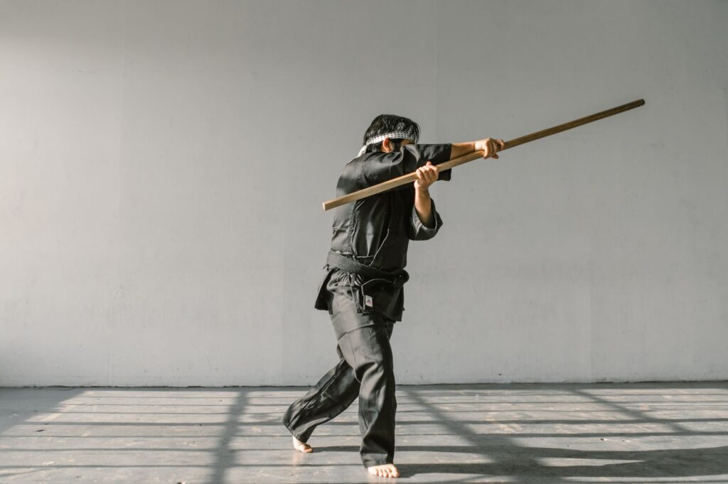 A martial artist in a dojo practicing with a bo staff, wearing a black gi.
