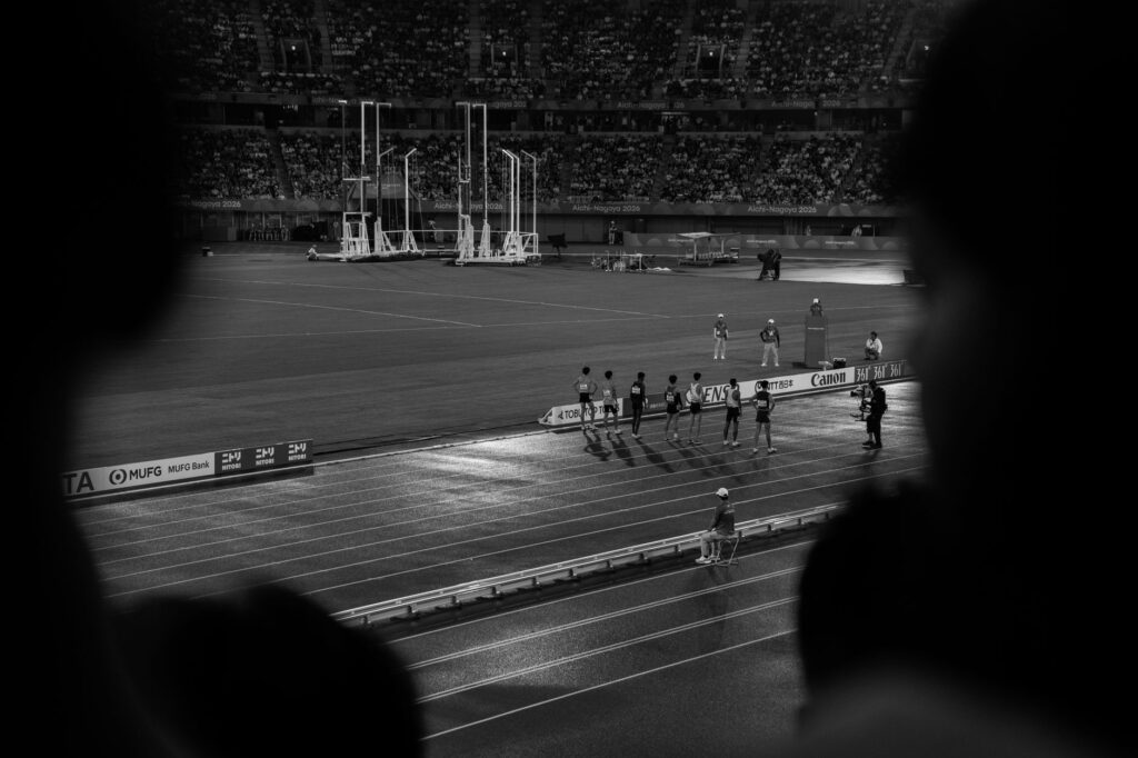 Black and white photo capturing track event at night in Aichi stadium, Japan.