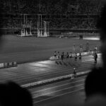 Black and white photo capturing track event at night in Aichi stadium, Japan.
