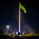 Majestic Saudi Arabian flag illuminated against the night sky, surrounded by cityscape lights in Riyadh.