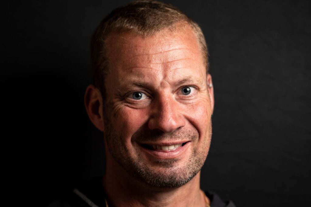 Close-up portrait of a smiling man against a black background, showcasing facial features.
